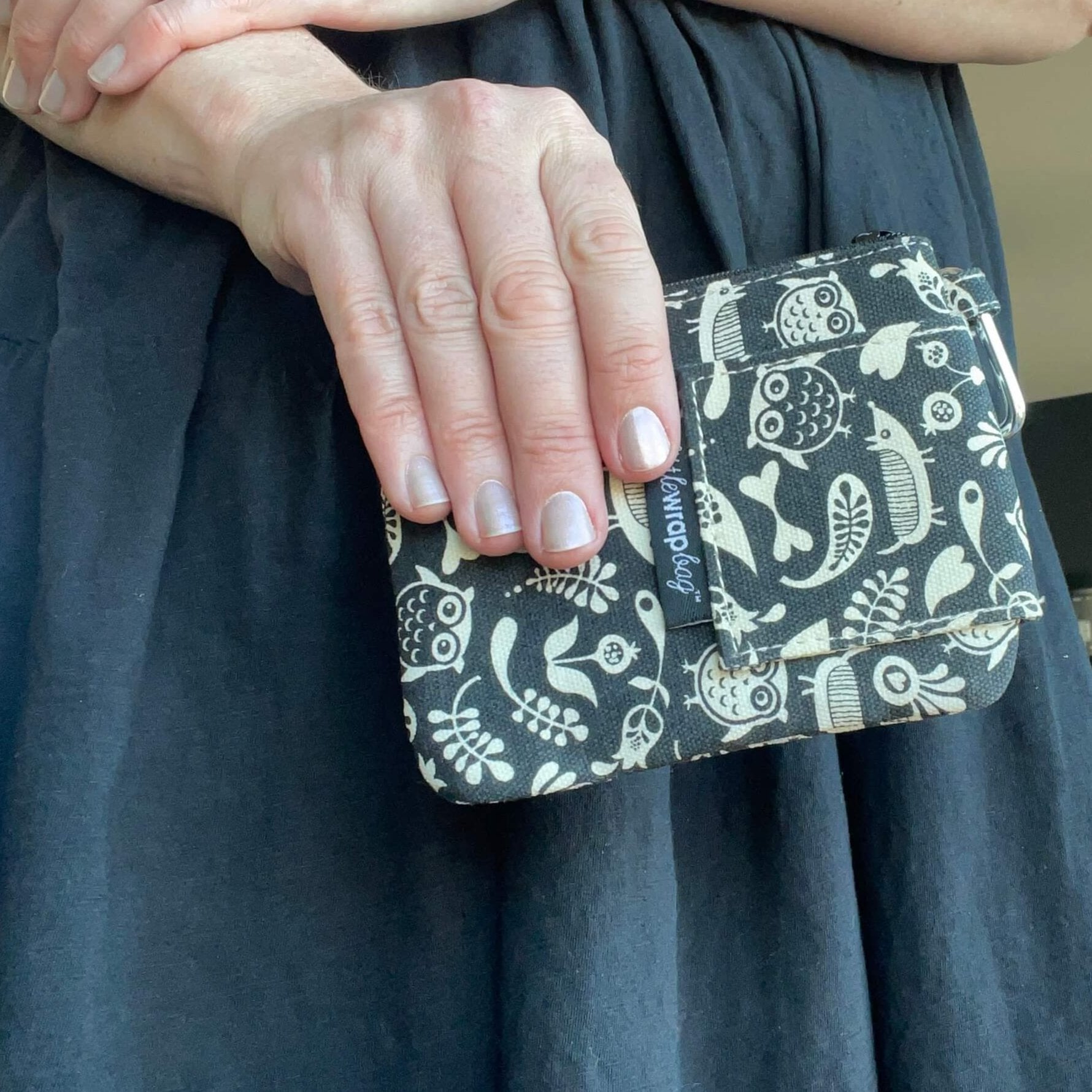 Womens hand holding a small Black purse with cream floral and owl pattern.
