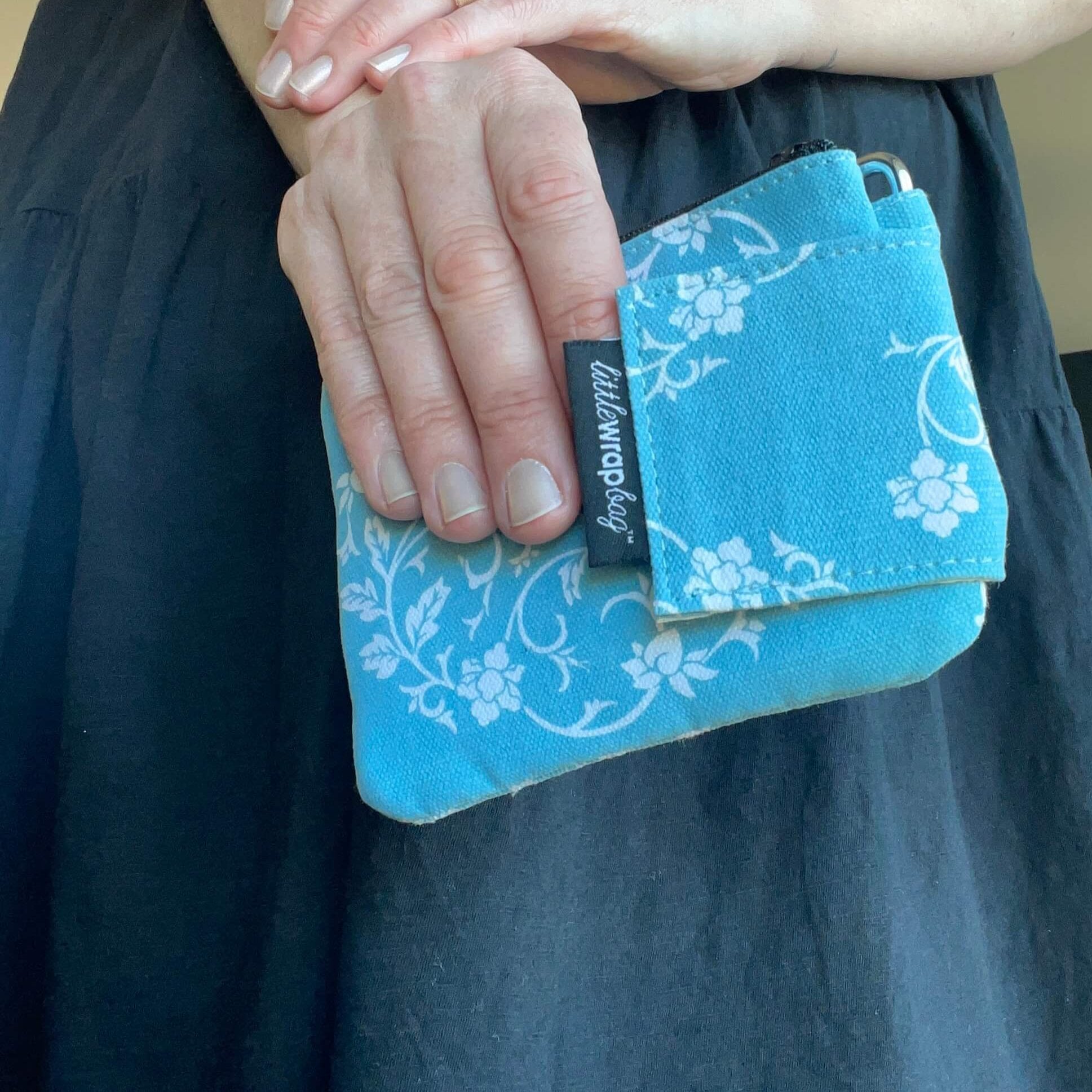 Womens hand holding a small blue purse with a white floral pattern.