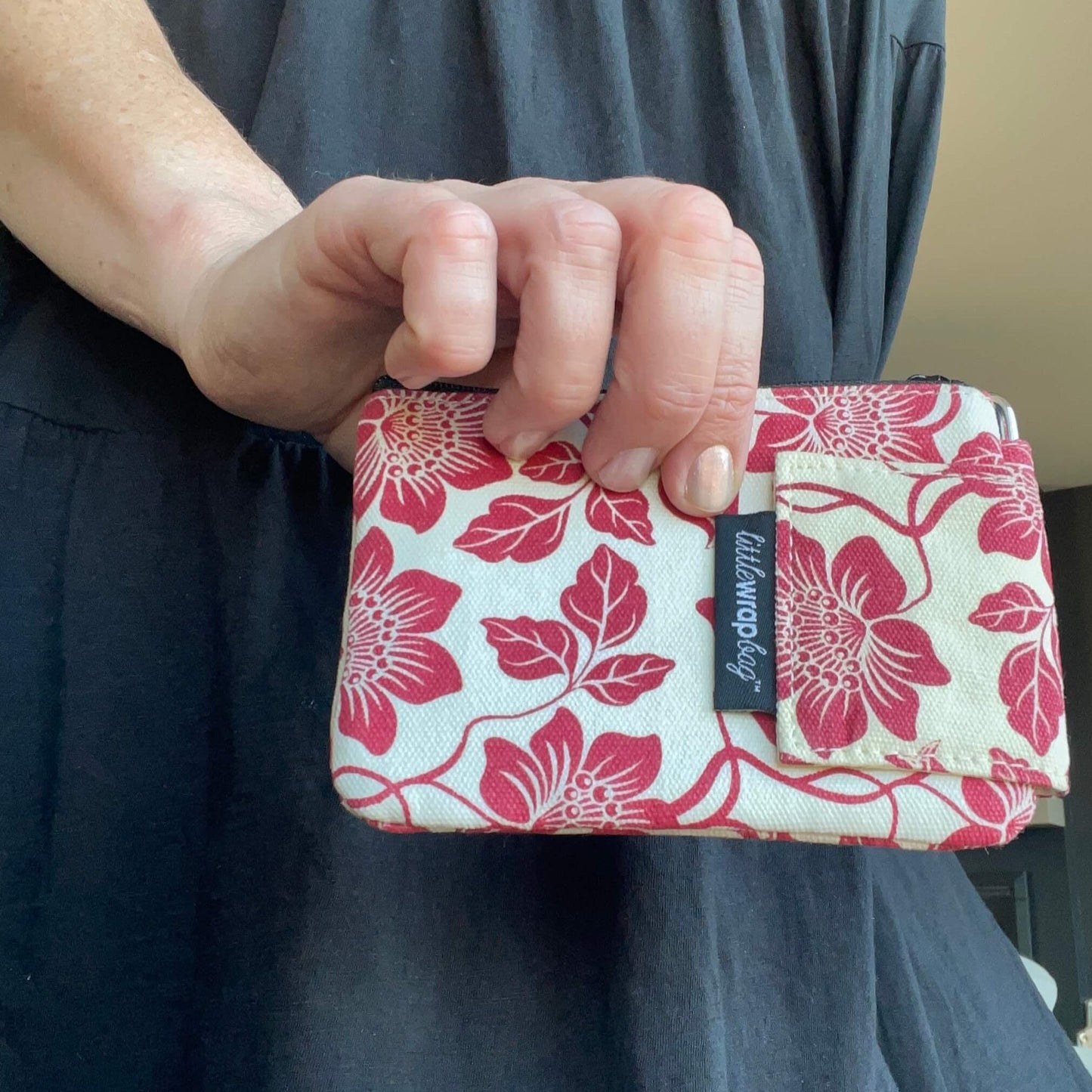 Womens hand holding a small cream purse with red floral pattern.