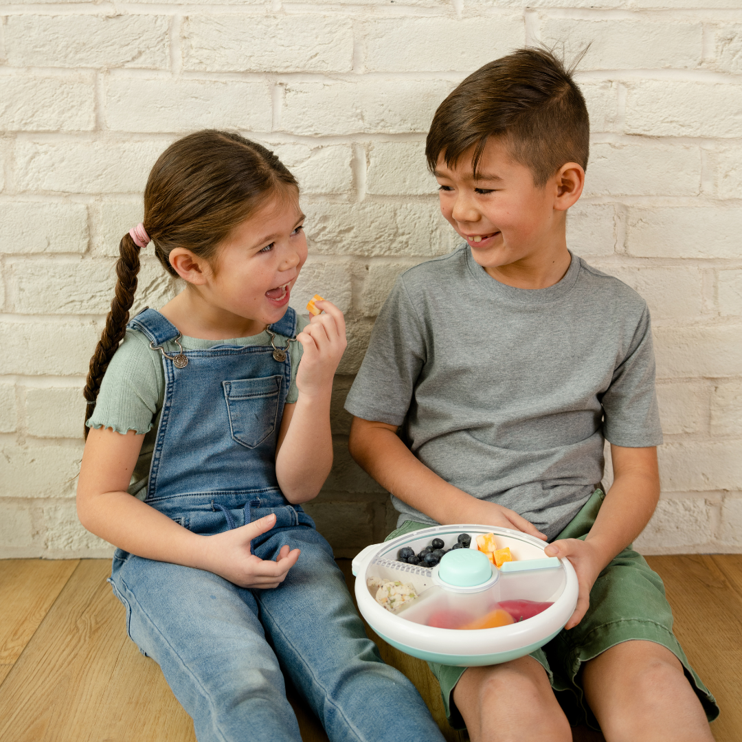 Two children sharing lunch from a Gobe snack spinner lunch box in pale blue and white.