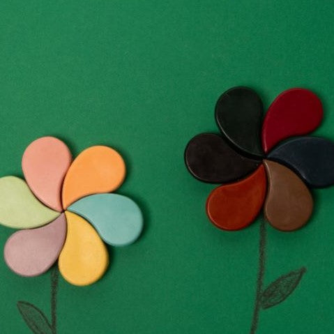 Petal shaped crayons laid out on green paper like flowers with stems drawn underneath.