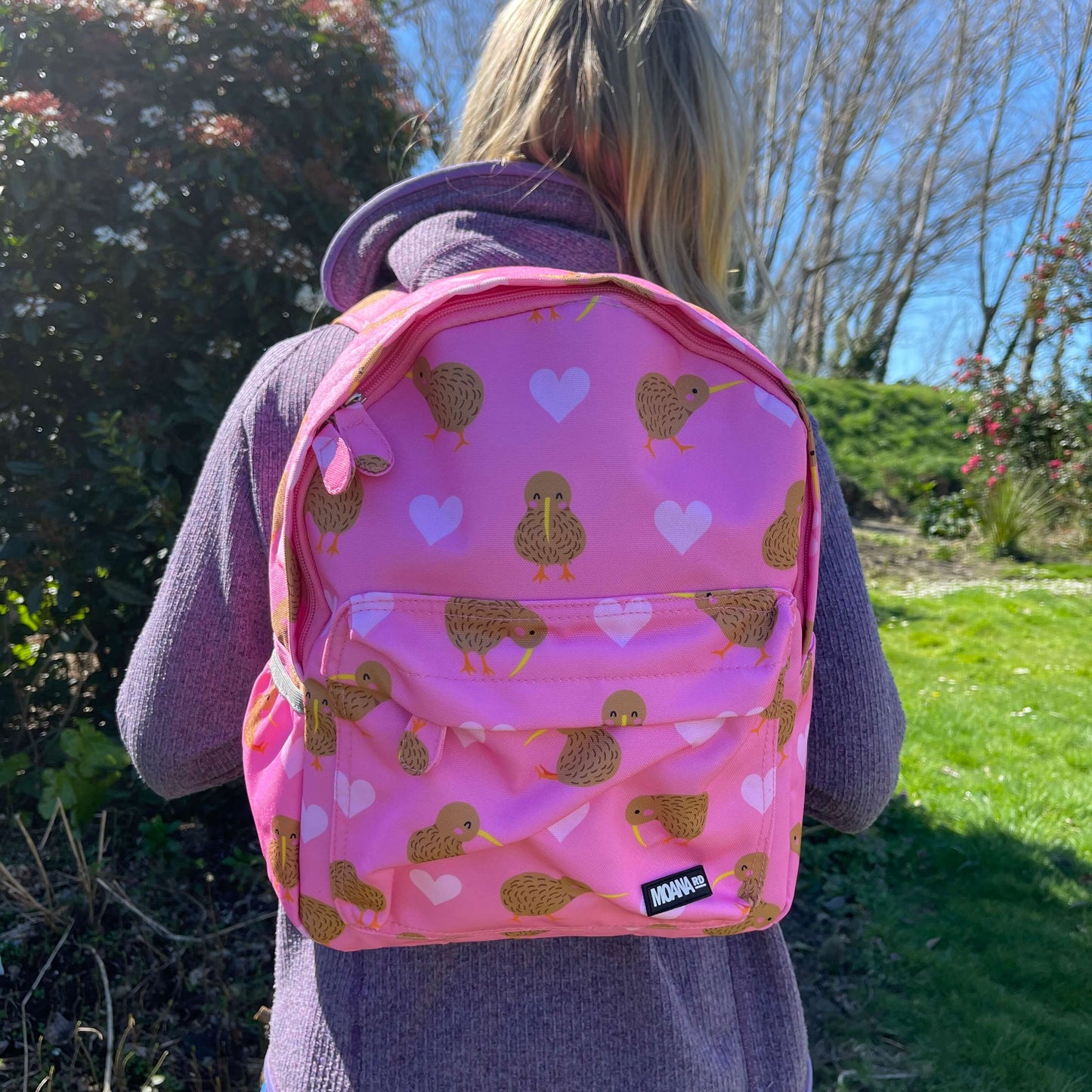 Child wearing a pink backpack with hearts and kiwi bird prints.