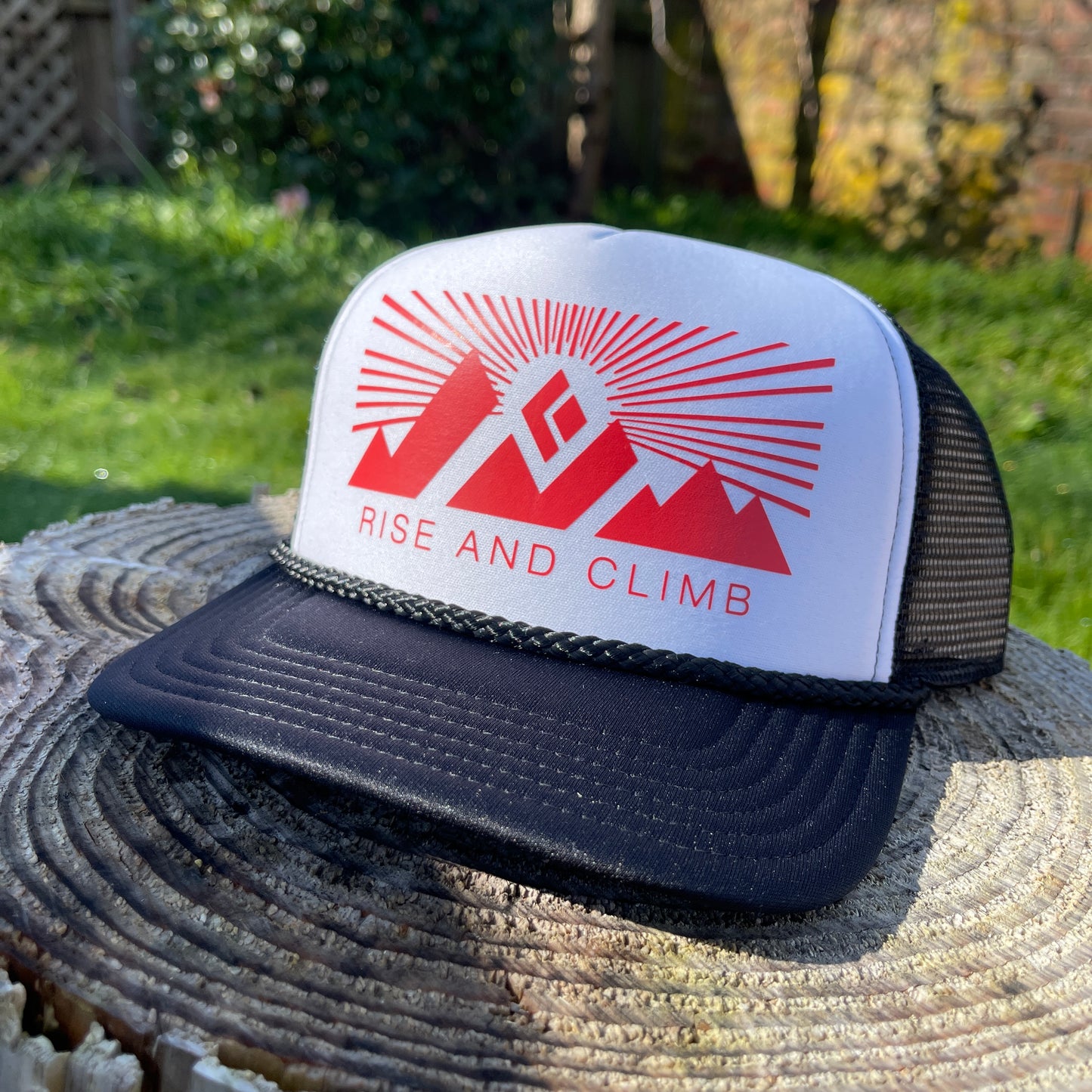 Black brim trucker hat with white front and red Rise and Climb logo.