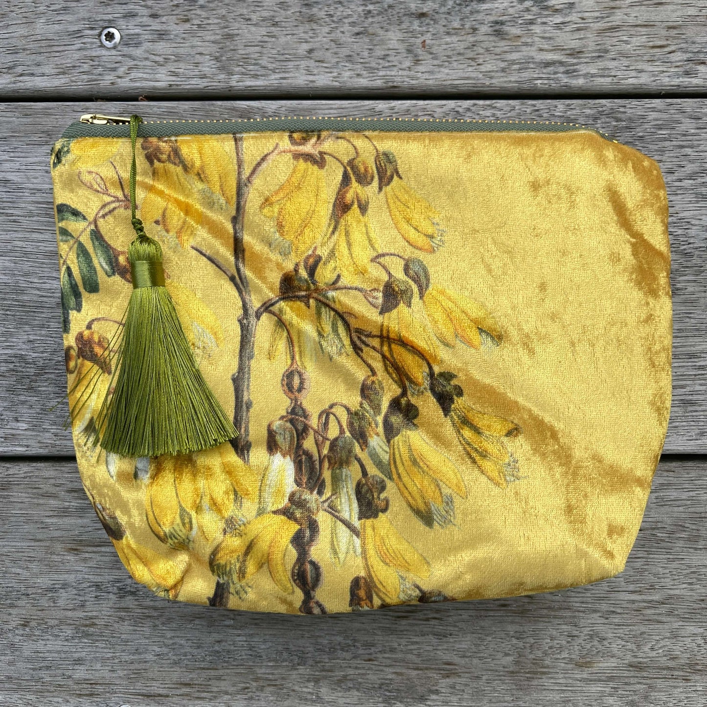 Golden velvet cosmetic bag with Kowhai flowers on it.