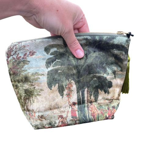 Persons hand holding a velvet cosmetic bag featuring a scene from a Joseph Dufour painting.
