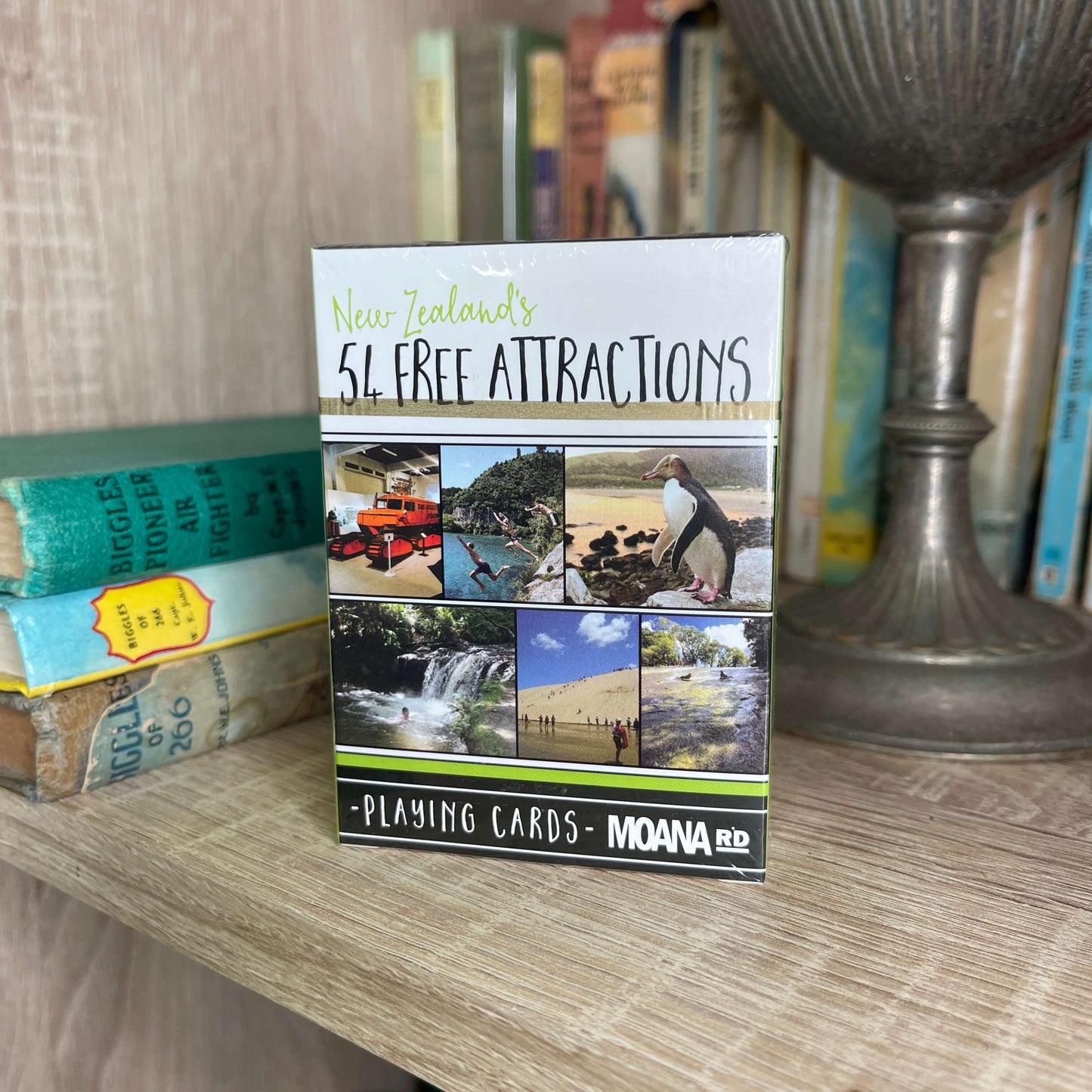 Pack of playing cards featuring NZ attractions sitting on a book shelf.