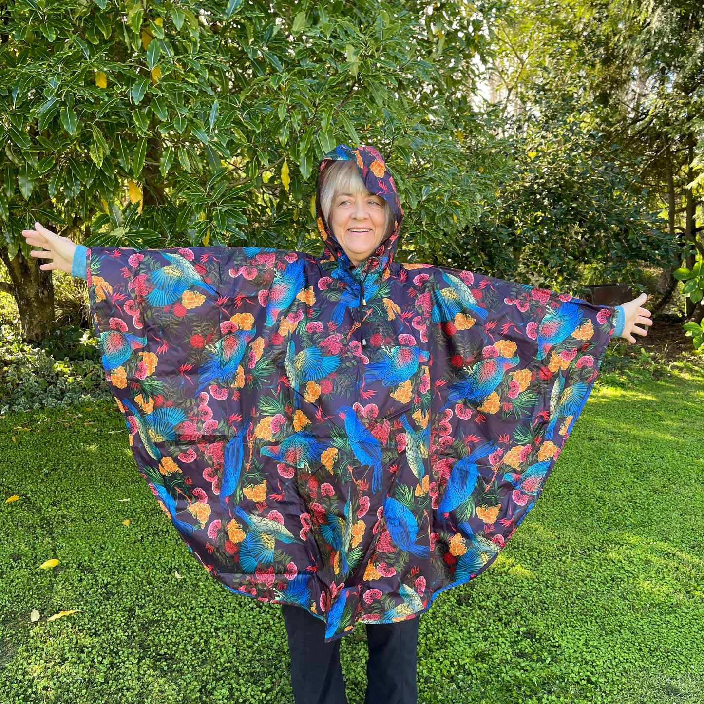 Woman wearing a rain poncho with birds and flower print on a deep aubergine purple background.