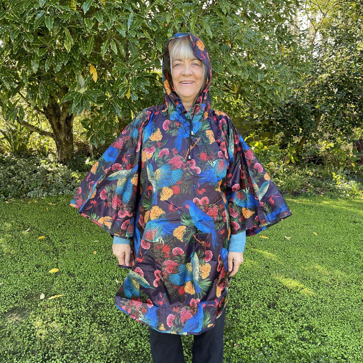 Woman wearing a rain poncho with birds and flower print on a deep aubergine purple background.
