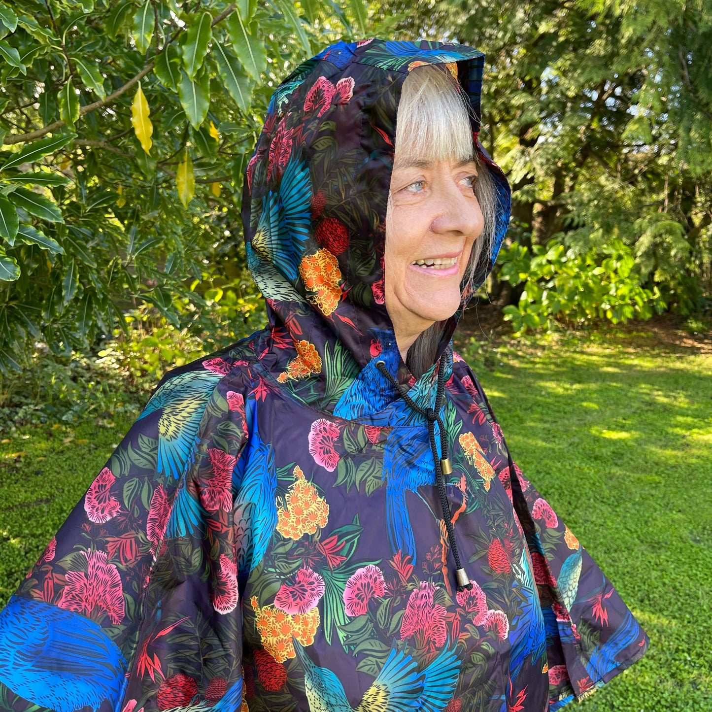 Woman wearing a rain poncho with birds and flower print on a deep aubergine purple background.