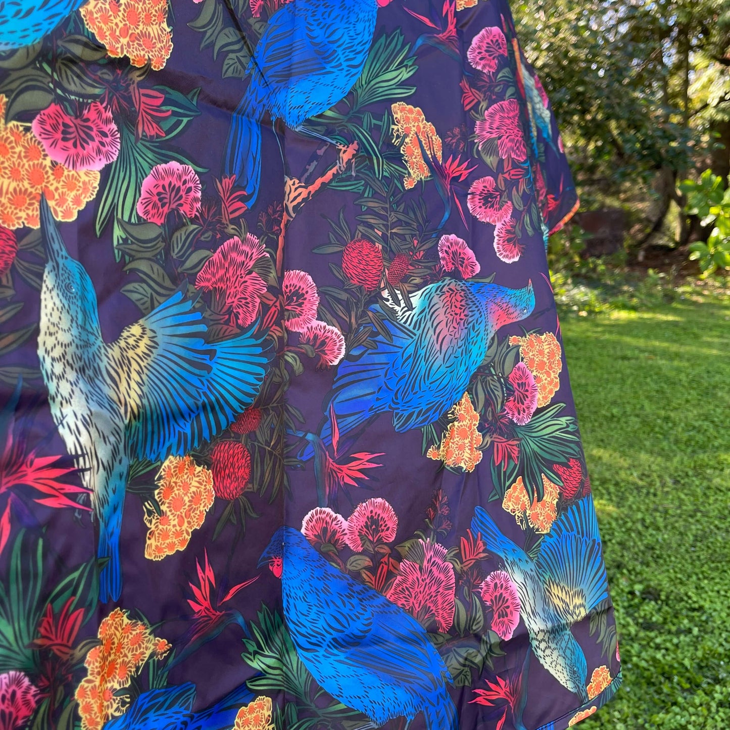 Close up of a rain poncho showing the floral & bird design on a deep aubergine purple background.