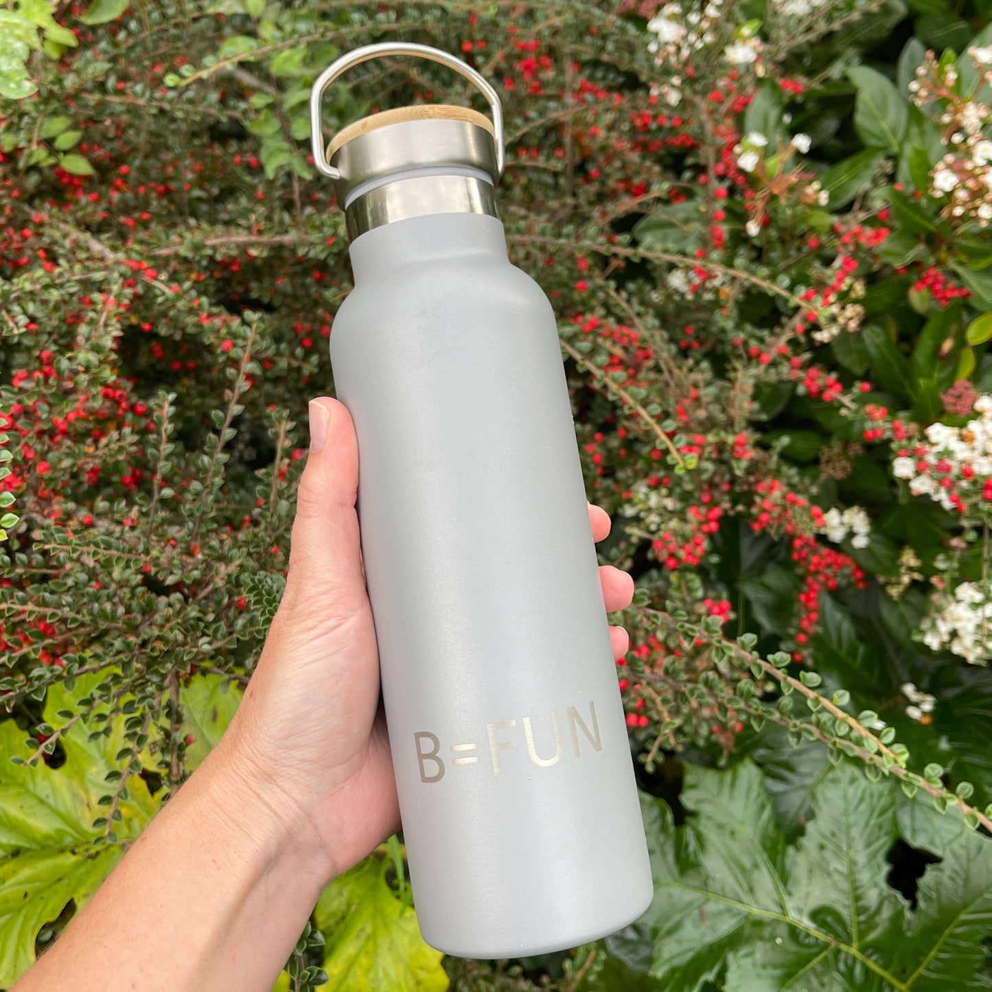 Womens hand holding a stormy grey stainless drink bottle with a bamboo cap and the words B=FUN engraved on it.