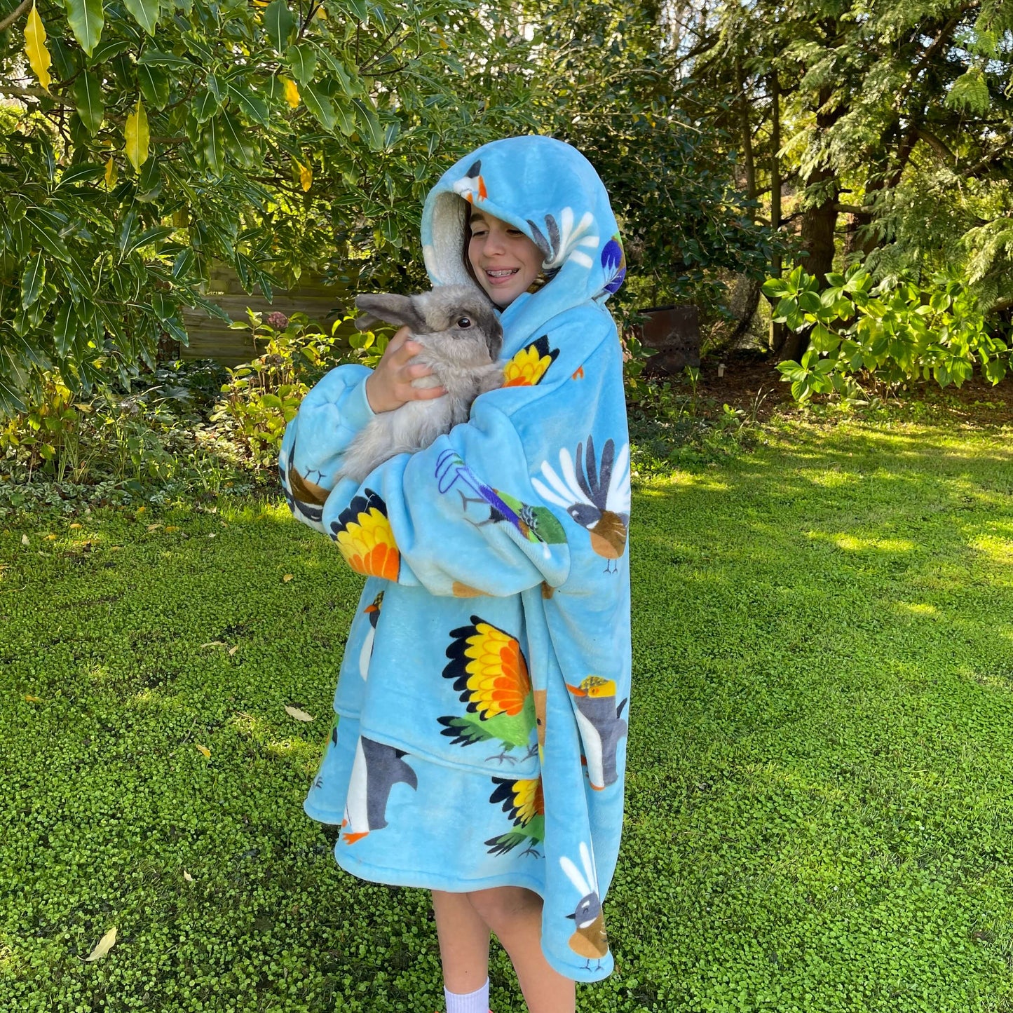 Young girl holding a bunny rabbit wearing an oversized blue hoodie with New Zealand birds printed on it.