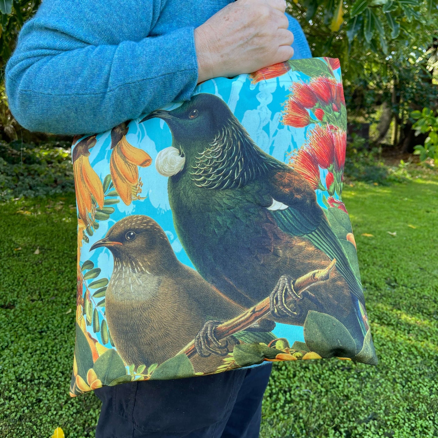 Close up of a woman with a tote bag over her arm. The tote features a Bellbird & Tui amongst Kowhai & Pohutukawa flowers.