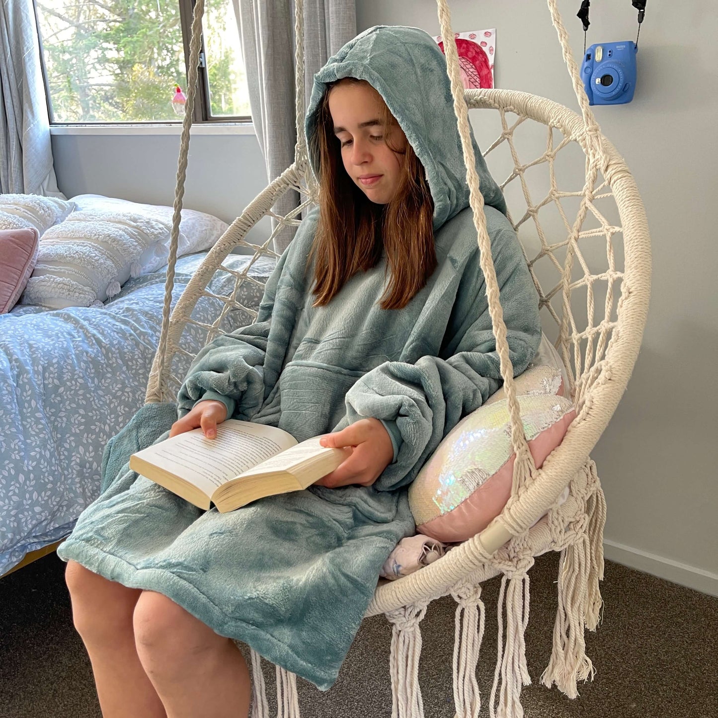Girl sitting in a swing chair reading a book wearing an oversized blue hoodie.