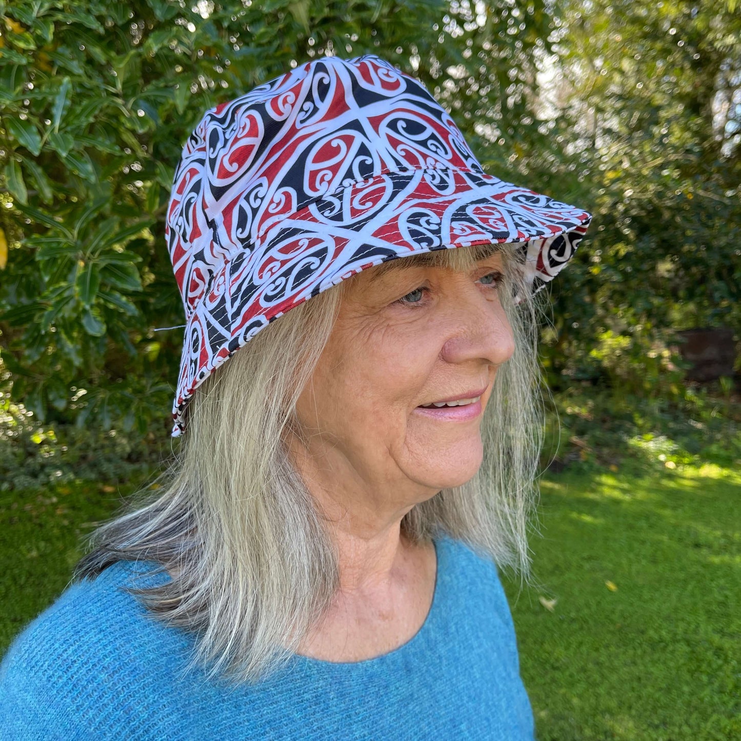 Woman wearing bucket hat with black, red & white maori koru design.