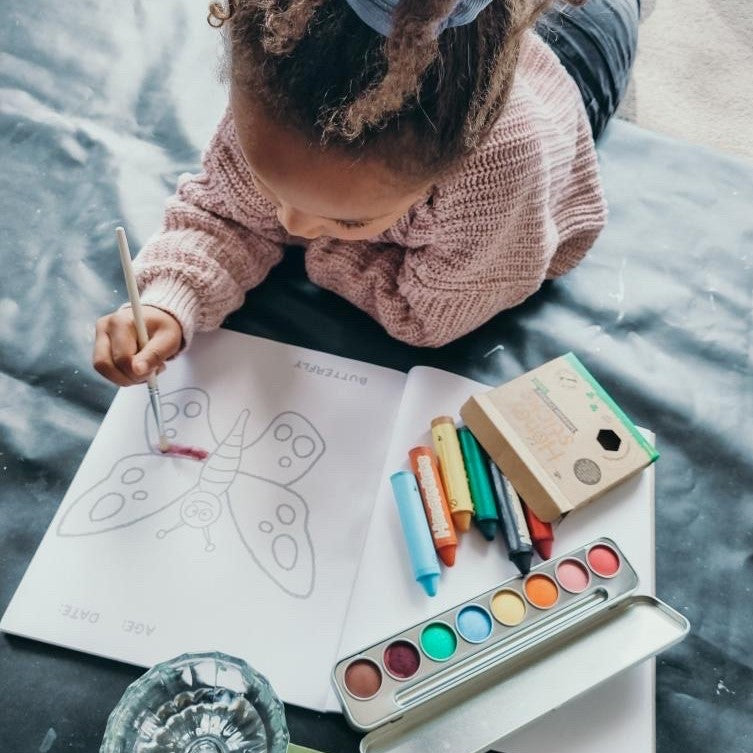 Child painting in a Honeysticks colouring book and crayons and paints.