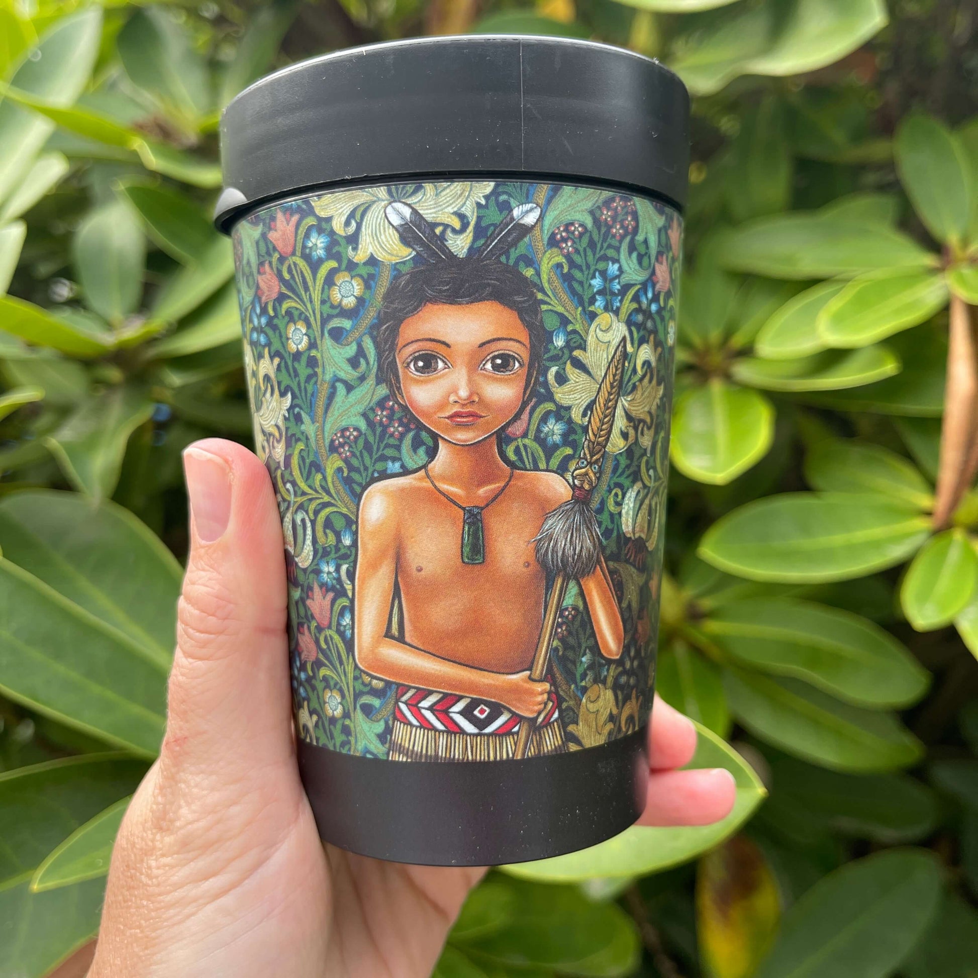 Black reusable coffee cup featuring a floral wrap and featuring an artists image of a young Māori boy holding a spear.