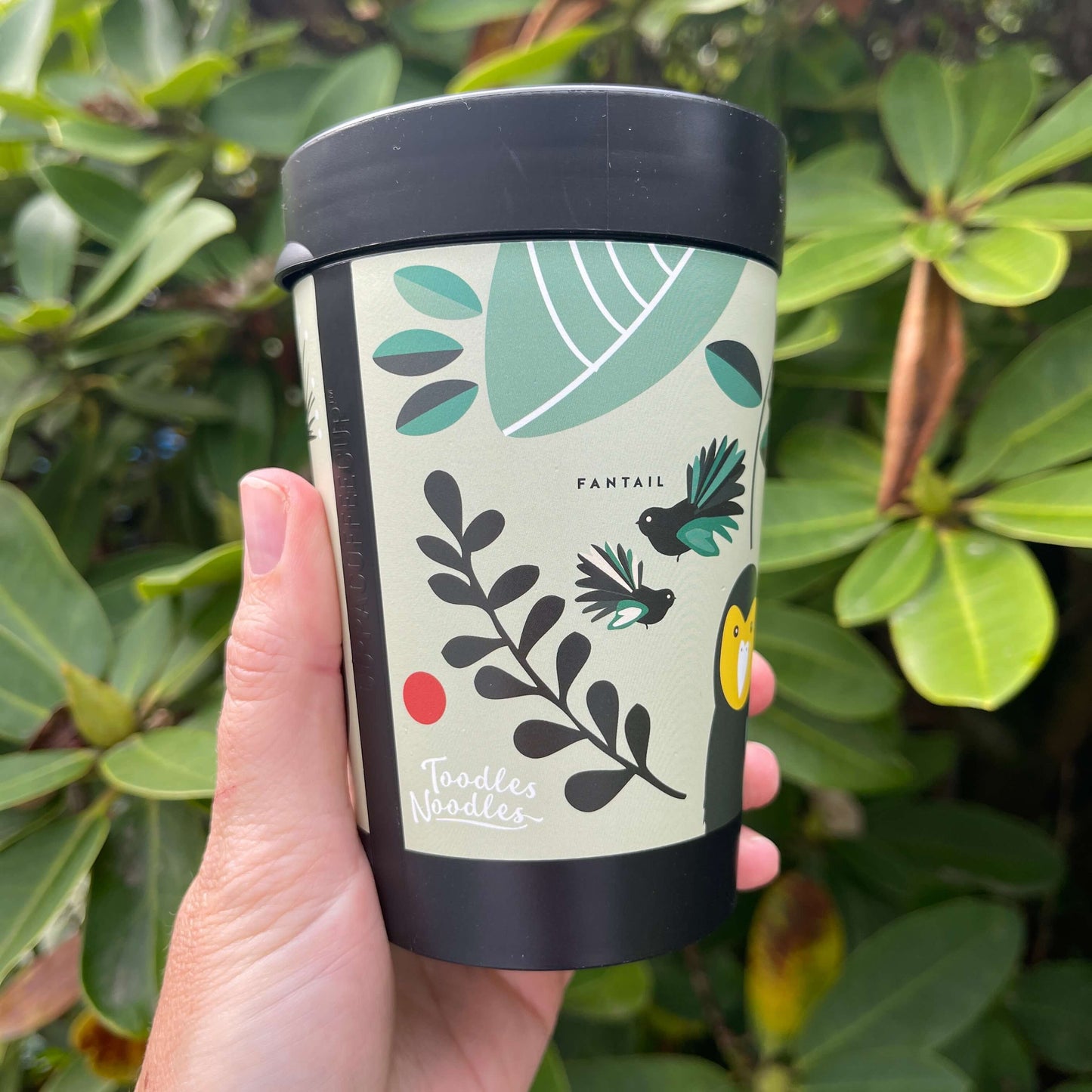 Black reusable coffee cup featuring New Zealand birds in a cartoon style on a minty green wrap background.