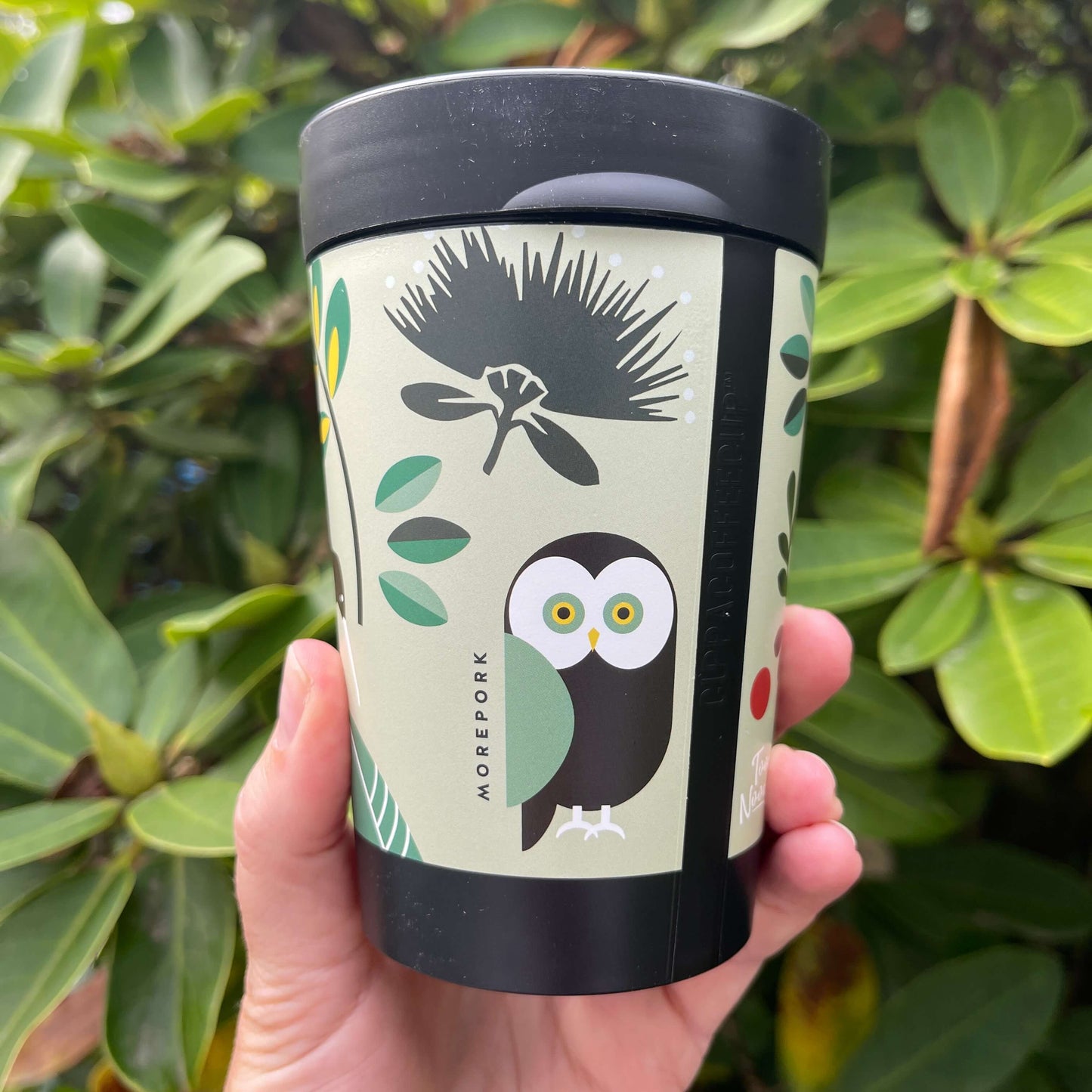 Black reusable coffee cup featuring New Zealand birds in a cartoon style on a minty green wrap background.