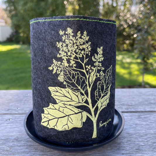Dark grey felt planter with light green Rangiora flower print and sitting in a grey dish.