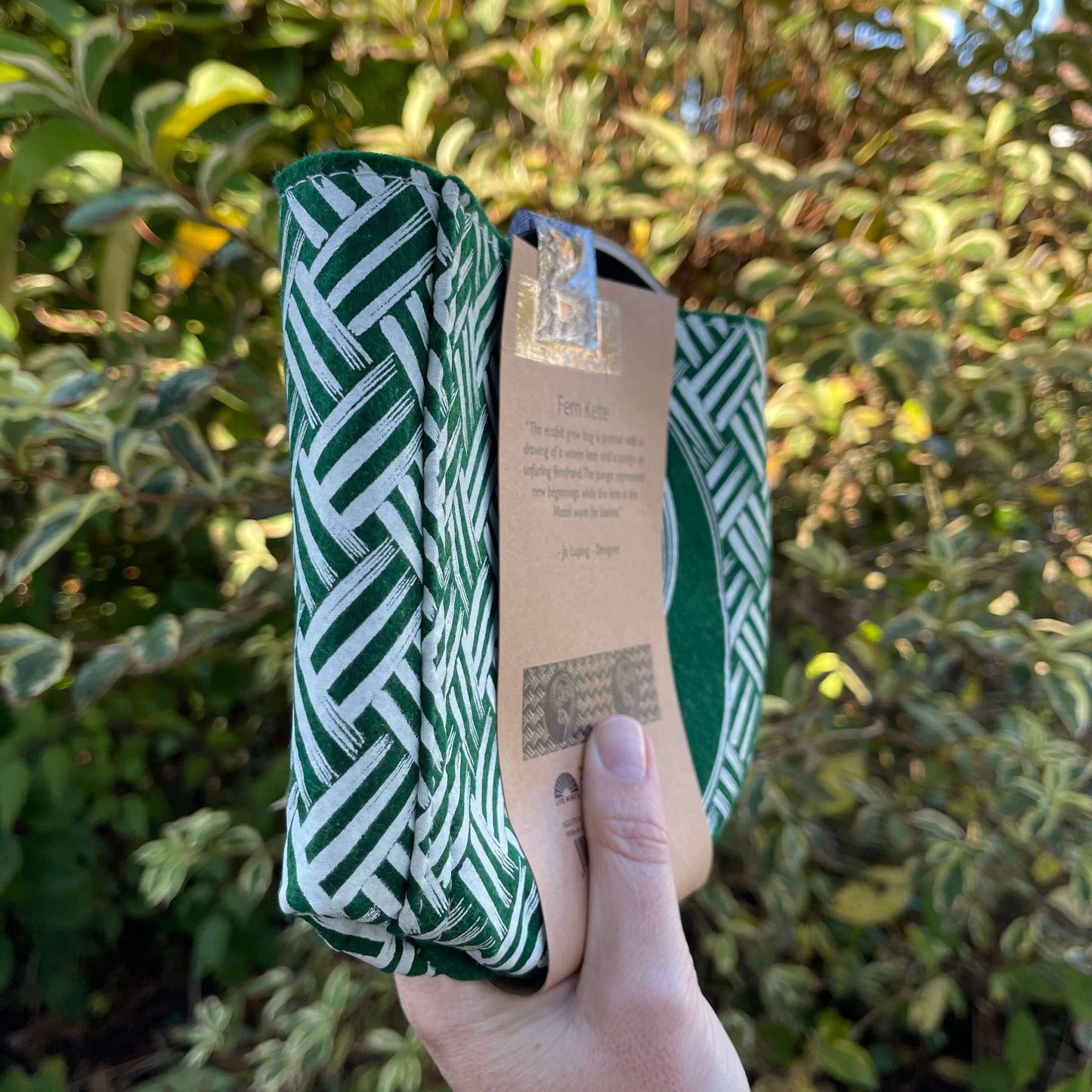 Green felt plant pot with white kete and ponga design, flat packed and wrapped with kraft paper.