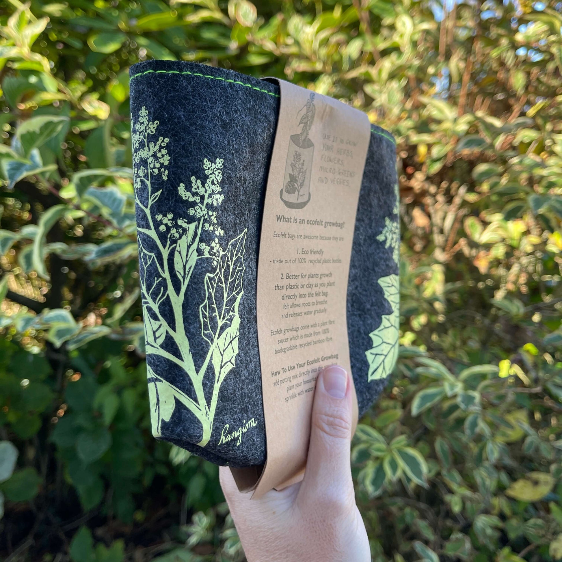 Dark grey felt planter with light green Rangiora flower print and sitting in a grey dish, flat packed and wrapped with kraft paper.