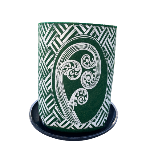 Green felt plant pot with white kete and ponga design, sitting in a dark grey saucer.