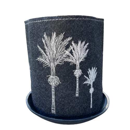 Dark grey felt planter with white Nikau trees printed on it sitting in a grey dish.