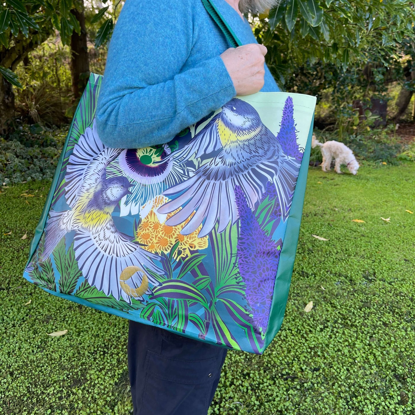 Woman with a tote bag over her arm. The vibrant coloured tote bag features Miromiro birds by artist Flox.