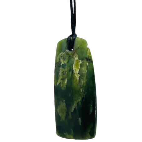 Greenstone freeform pendant on a black wax cord draped over a rock.