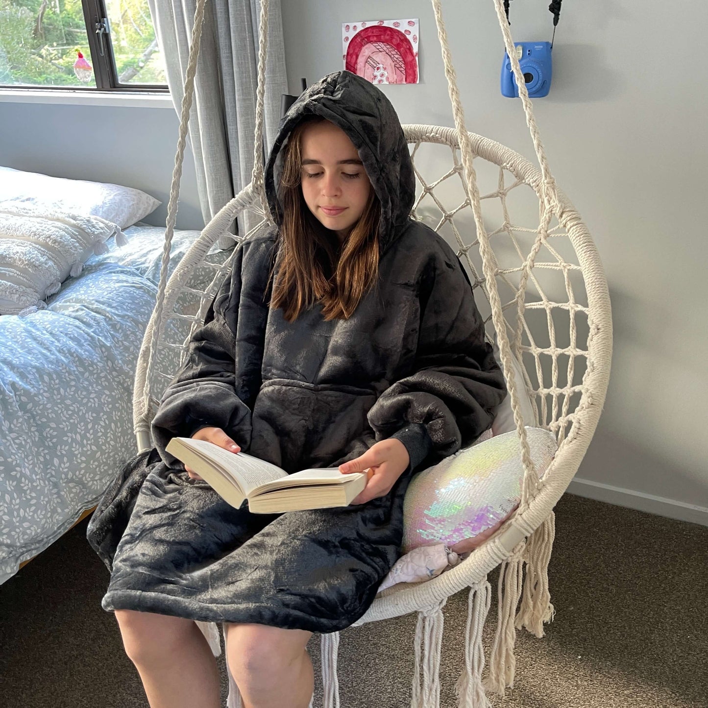 Girl sitting in a swing chair reading a book wearing an oversized grey hoodie.