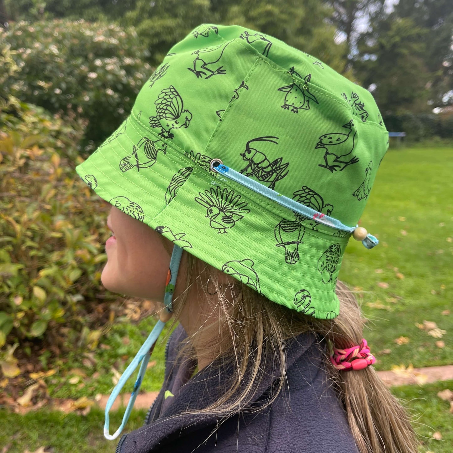 Girl wearing a Bright green bucket hat with black outlines of Native New Zealand animals.