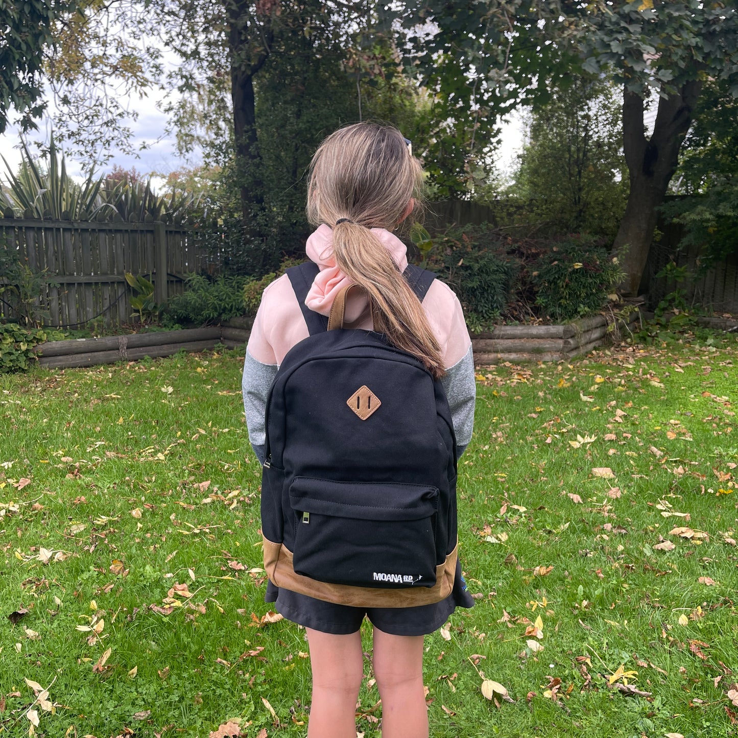 Girl wearing black & tan backpack with 2 zippered compartments.