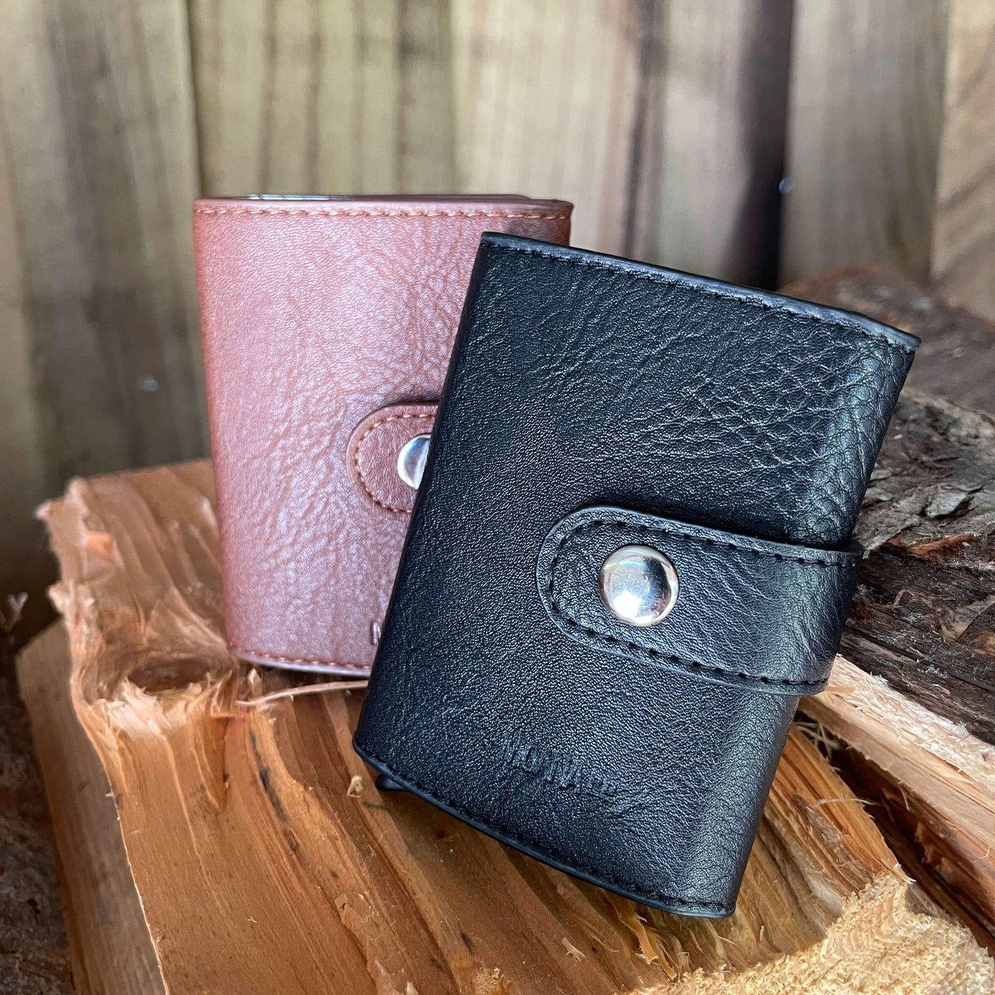 Small pocket wallets in tan & black sitting on a piece of firewood.