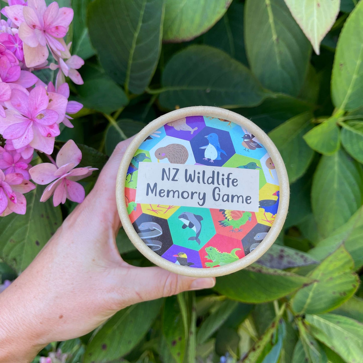 Women's hand holding cardboard tube with an NZ Wildlife Memory Game inside.