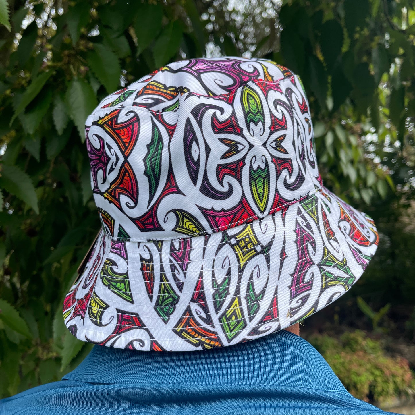 Back of mans head wearing a brightly coloured bucket hat with koru patterns.