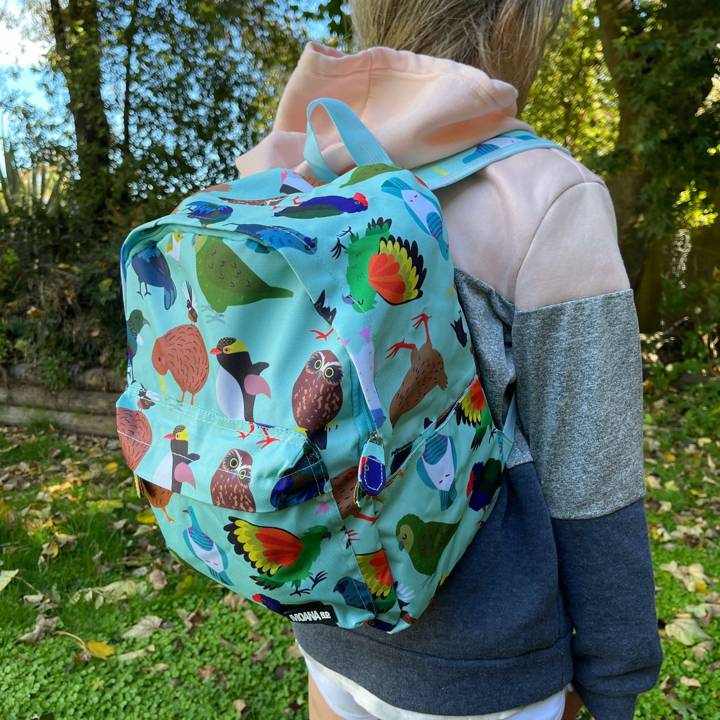 Child wearing a minty green backpack covered in bright prints of New Zealand birds.