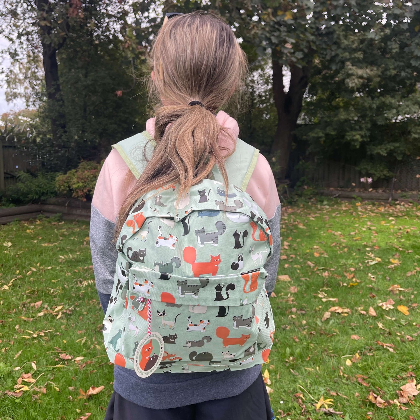 Girl wearing a mint green backpack with assorted coloured cats printed on it.