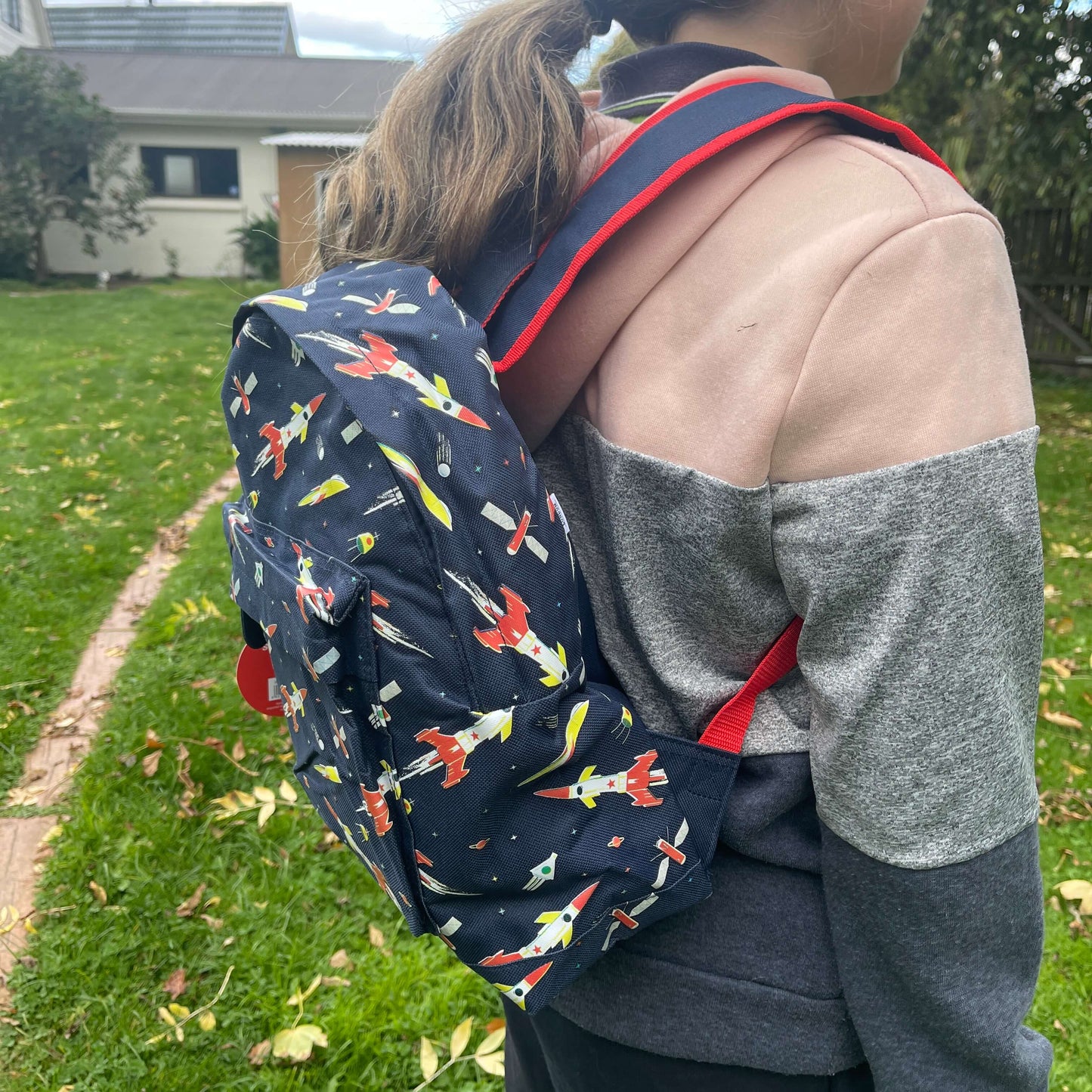 Girl wearing a navy blue backpack with rockets and space ships printed on it.