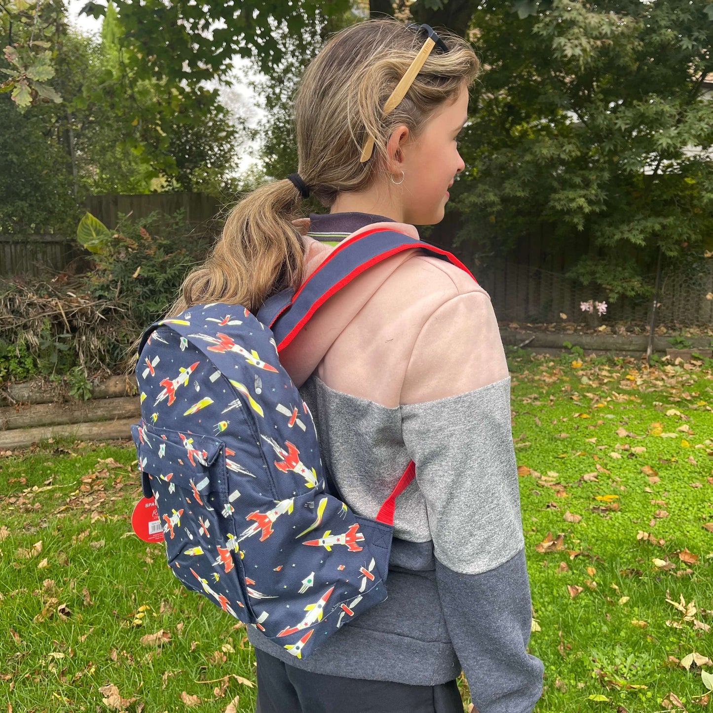 Girl wearing a navy blue backpack with rockets and space ships printed on it.
