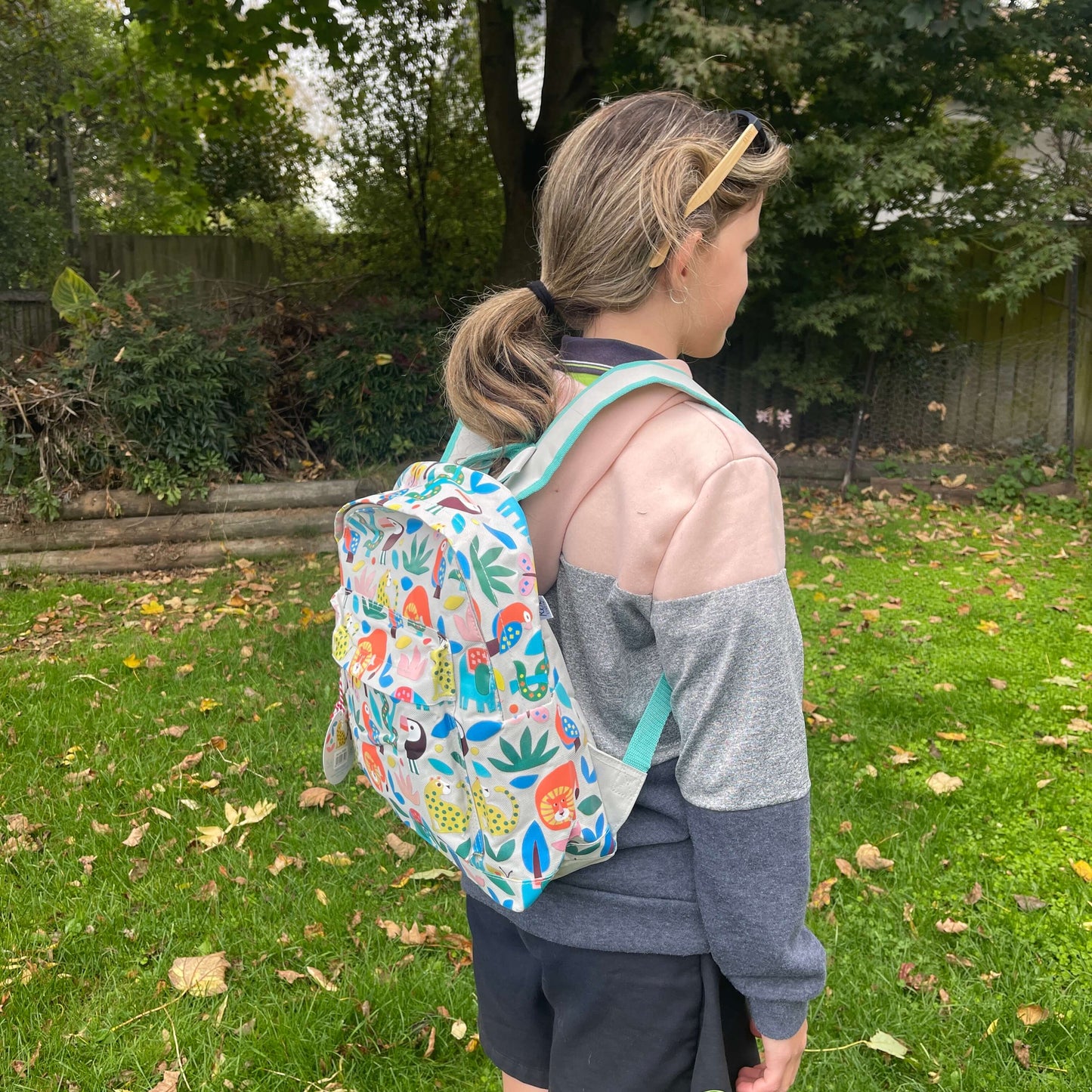 Girl wearing a backpack with bright jungle animals printed on it.