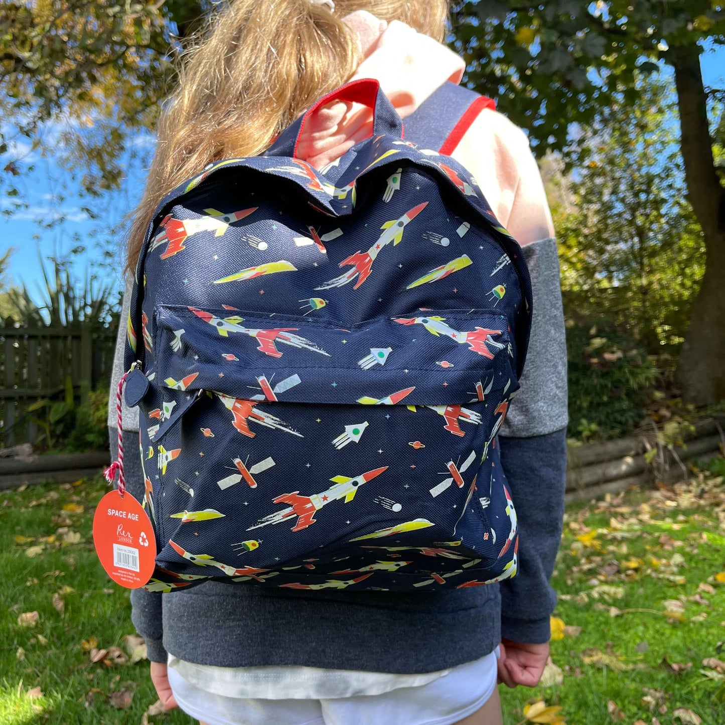 Girl wearing a navy blue backpack with rockets and space ships printed on it.