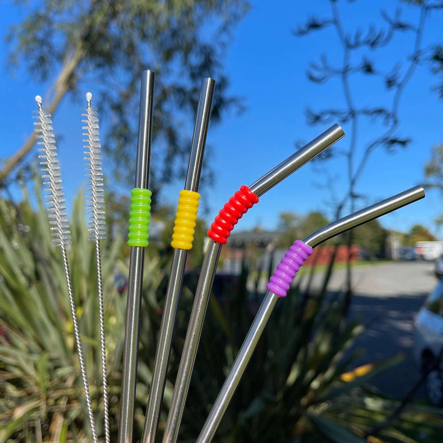 Set of 4 stainless steel reusable straws and 2 cleaning brushes with a beautiful blue day in the background.