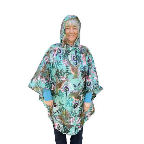 Woman wearing a rain poncho with birds and flower print on a light blue background.