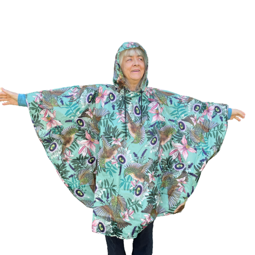 Woman wearing a rain poncho with birds and flower print on a light blue background.