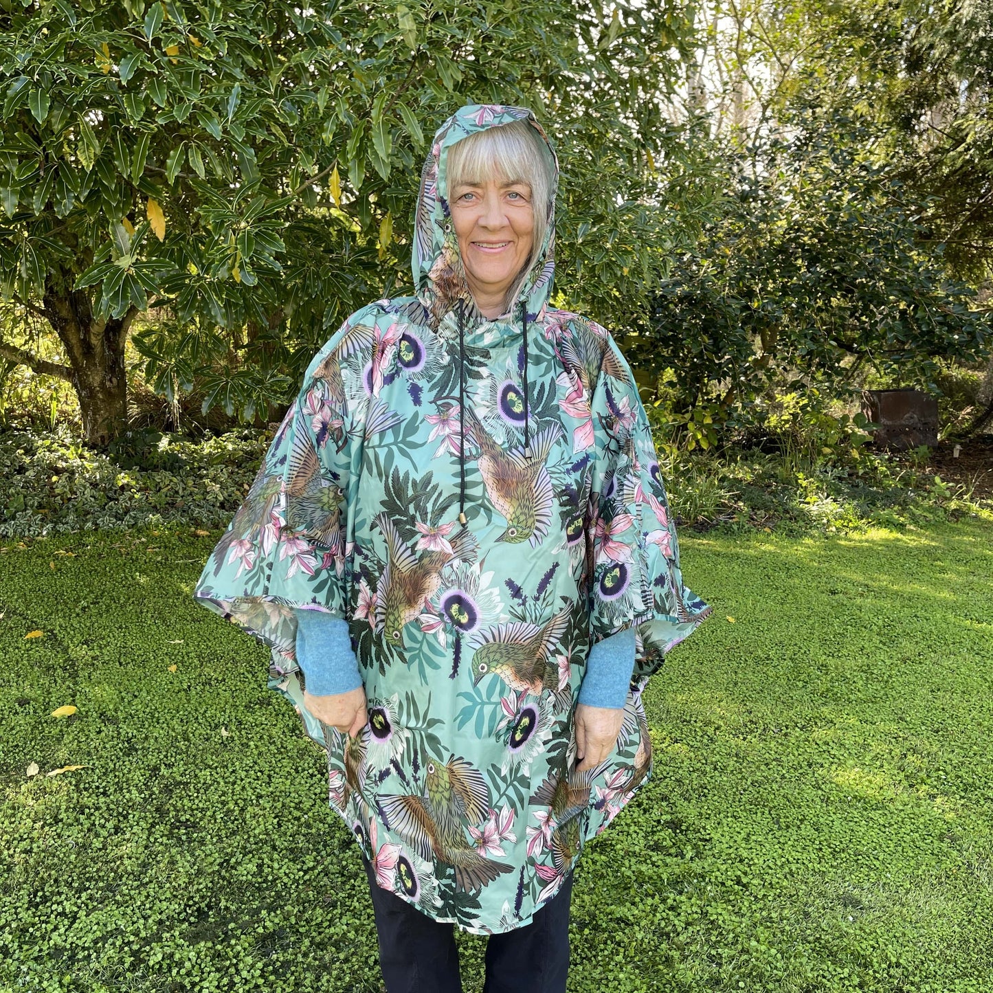 Woman wearing a rain poncho with birds and flower print on a light blue background.