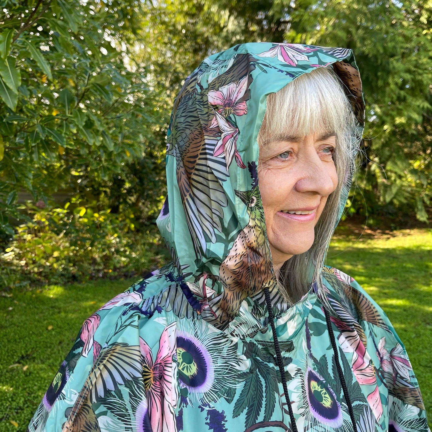 Woman wearing a rain poncho with birds and flower print on a light blue background.