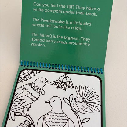 An open children's coloring book or activity booklet with a green cover page showing bird-related text and a black-and-white Kererū bird illustration on the inside cover.