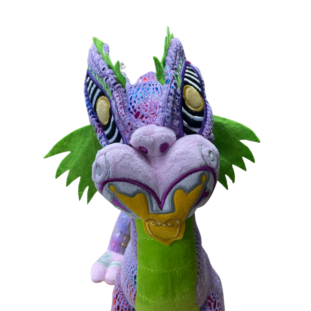 Close up of the face of a plush toy Taniwha with purple and green base and shimmery scales in rainbow colours. Embroidered koru designs feature on the face a golden tongue.