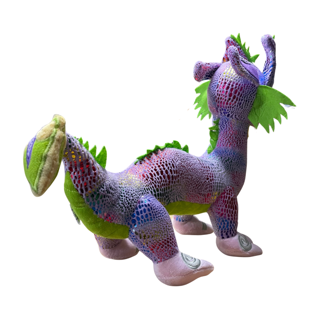 Plush toy Taniwha with purple and green base and shimmery scales in rainbow colours. Embroidered koru designs feature on the feet, tail and face.